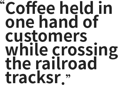 " Coffee held in one hand of customers while crossing the railroad tracks "